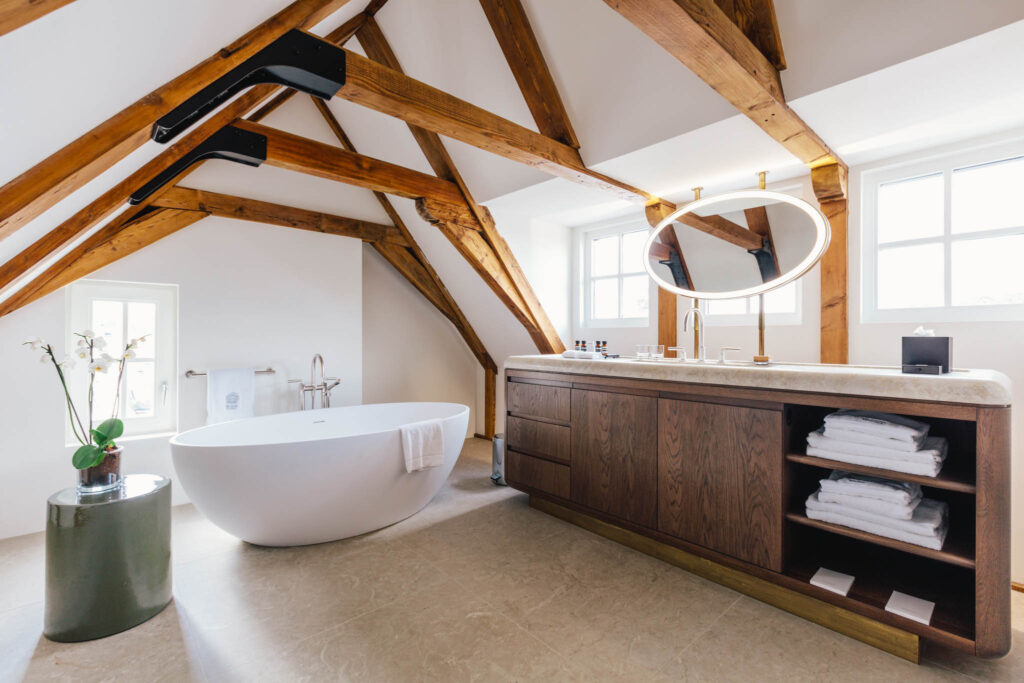 Bathroom in a Loft style suite at boutique hotel The Dylan Amsterdam, with a fee standing bath, exposed beams and a marble and wood console.