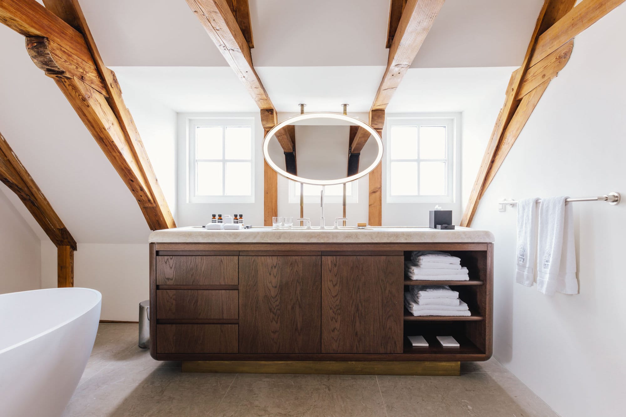 Bathroom in a Loft style suite at boutique hotel The Dylan Amsterdam, with a fee standing bath, exposed beams and a marble and wood console.