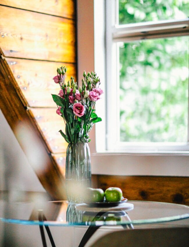 A table with a vase with pink rose flowers and three green apples on it, in a room at luxury boutique hotel The Dylan Amsterdam, member of The Leading Hotels of The World.