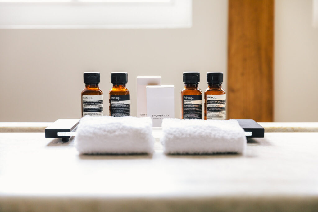 Shampoo, conditioner and bathsoap from Aesop and a shower cap, cotton buds and white hand towels, in a bathroom of a room in luxury boutique hotel The Dylan Amsterdam, member of The Leading Hotels of The World.