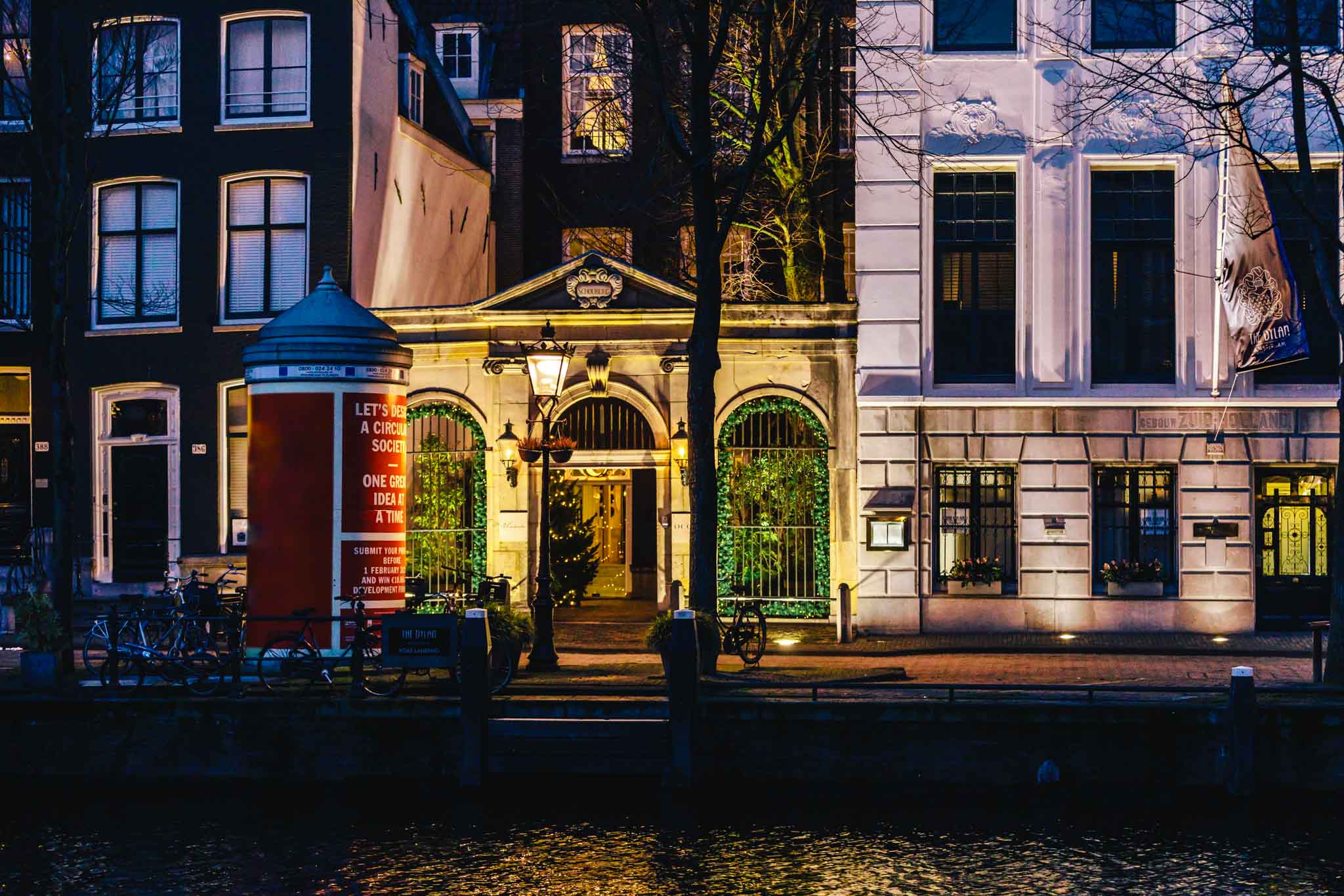 The entrance gate of luxe boutique hotel The Dylan Amsterdam, member of LHW by night with Christmas decorations reflecting on the canal water of Keizersgracht in Amsterdam