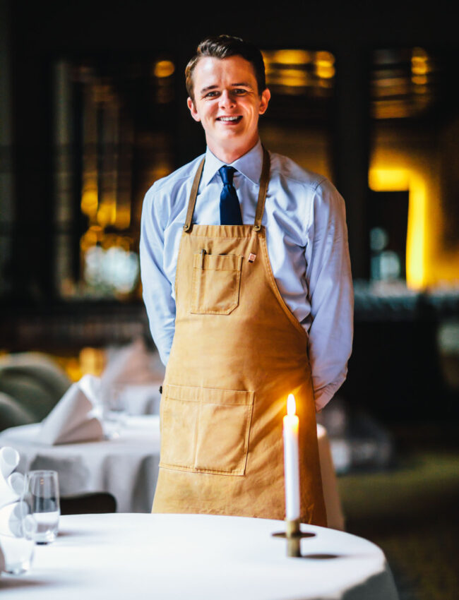 Jasper van Amerongen, assistant sommelier at Restaurant Vinkeles, posing next to a set-up table at Michelin-starred Restaurant Vinkeles in luxury boutique hotel The Dylan Amsterdam, part of The Leading Hotels of The World